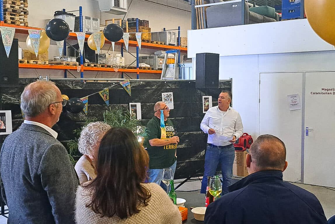 Toespraak tijdens het pensioenfeest van Dolmans-medewerker Henk, met collega's die toekijken in een feestelijk versierde bedrijfshal